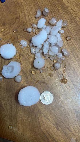 Hail stones on a table along with a quarter. Most are smaller than the quarter but a few are larger.