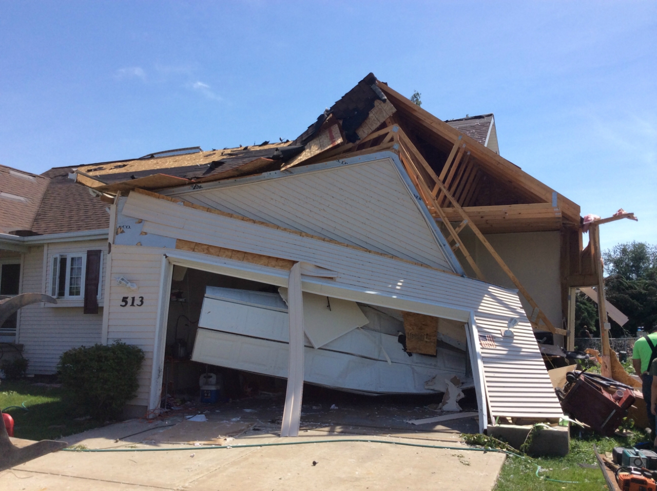 Photo showing damage from a tornado near Earlville. A house has a garage with a collapsed wall, a damaged roof, and a blown in garage door.