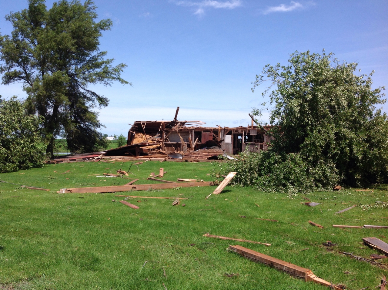 Photo showing damage from a tornado near Grant Park. A farm outbuilding has been damaged with collapsed walls and debris spread across a yard.