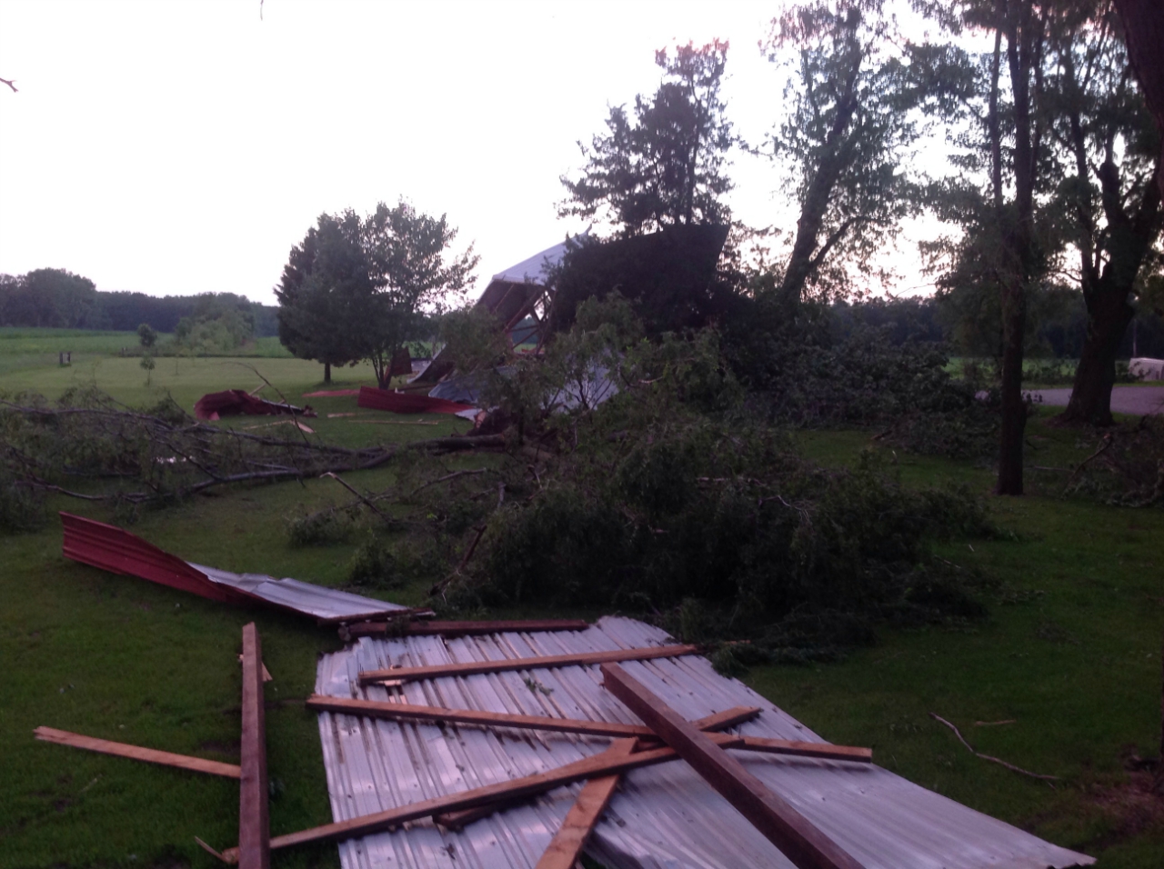 Photo showing damage from a tornado near De Motte. Debris from a farm outbuilding is spread across a yard and field.