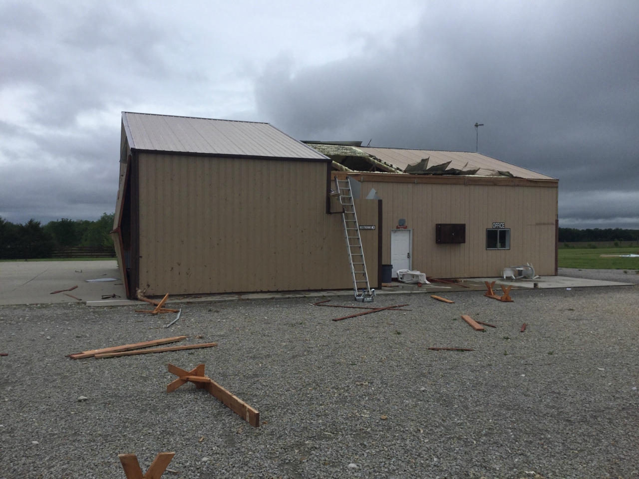 Photo of Damage to hanger building with roof panels removed and window/door blown out.