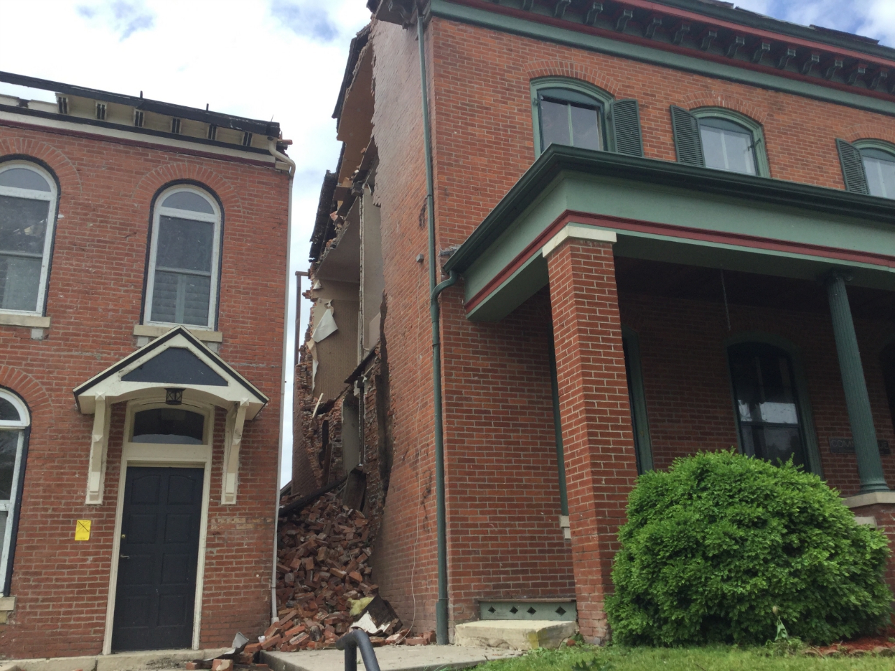 Photo of brick house with roof and side wall damage.