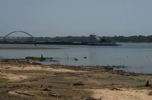Photo of a barge passing sandbars on Ohio River with the Interstate 24 bridge in background